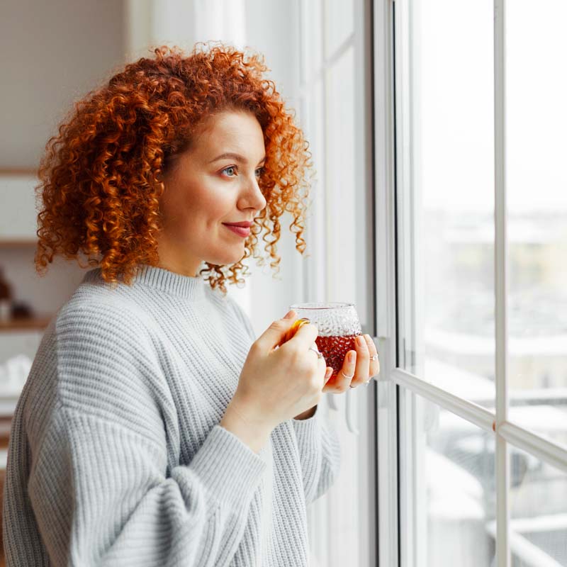 femme tenant une tisane face à la fenetre en hiver